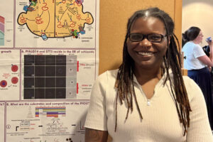 Mya A smiling person with dreadlocks stands in front of a scientific research poster about yeast biology and protein composition.